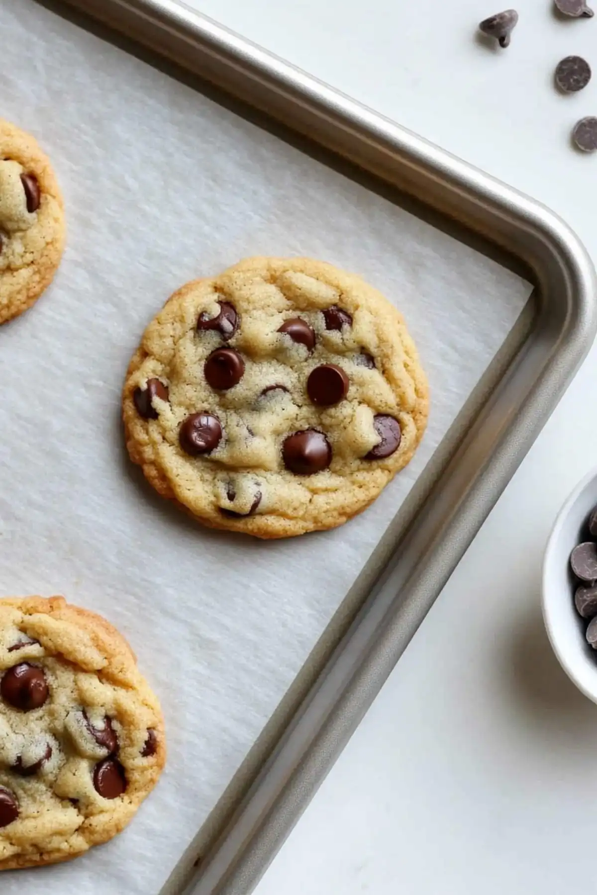 Freshly baked gluten-free dairy-free chocolate chip cookies cooling on a baking sheet lined with parchment paper