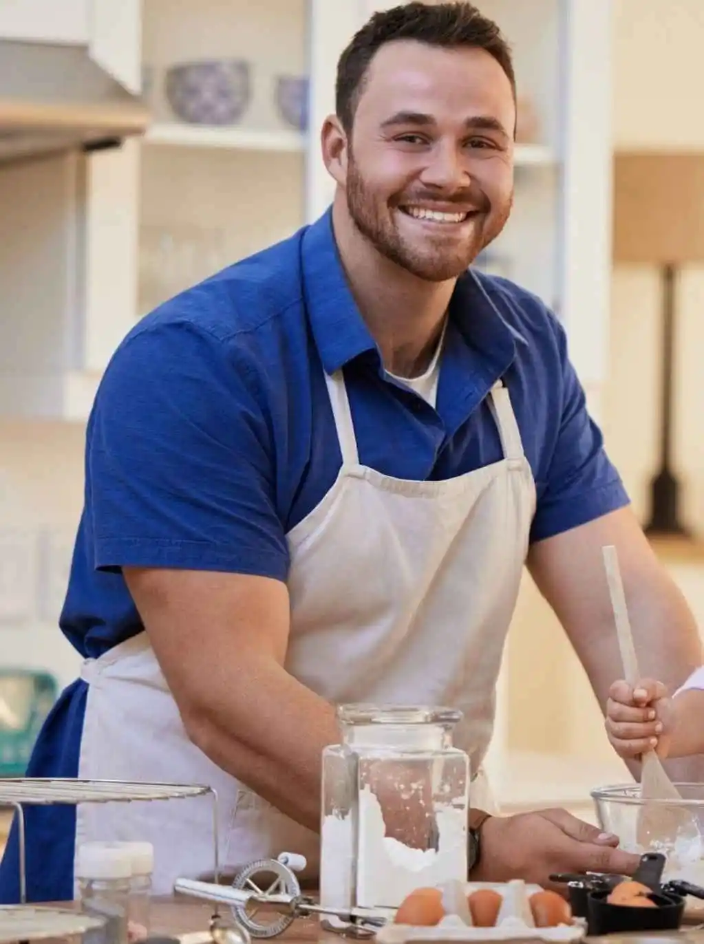 Contact I Need Recipe – Kevin smiling in the kitchen wearing an apron, preparing a meal
