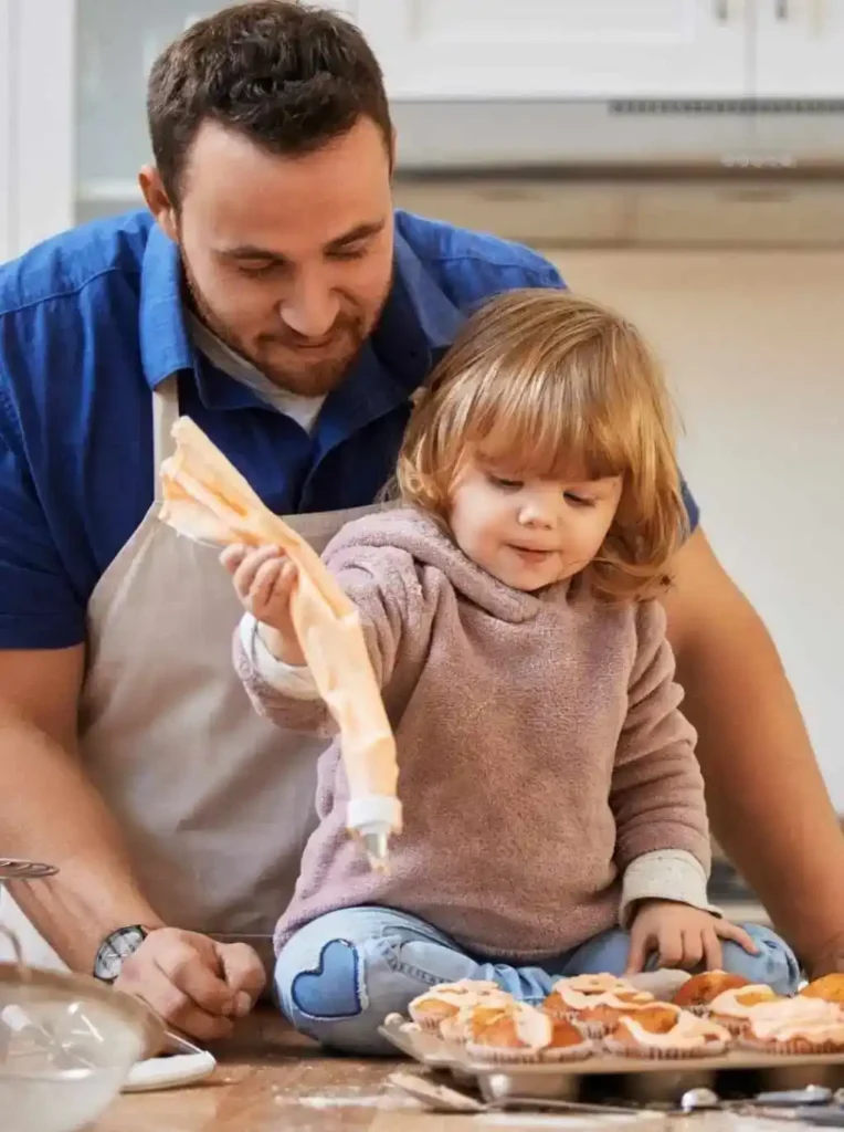 Father helping his young daughter decorate cupcakes with frosting in a warm family kitchen