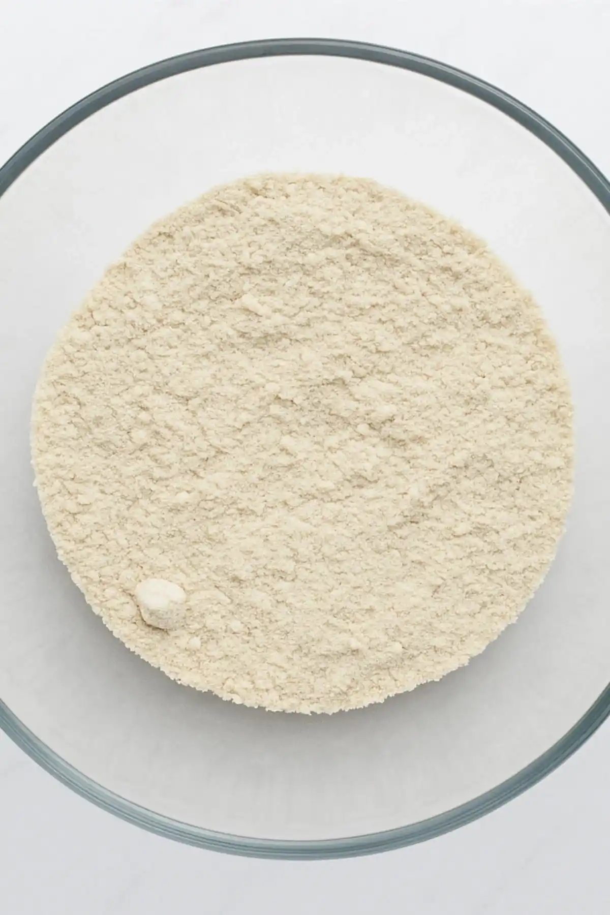 Mixed dry ingredients for gluten free sugar free bread in a clear glass bowl on a white background.