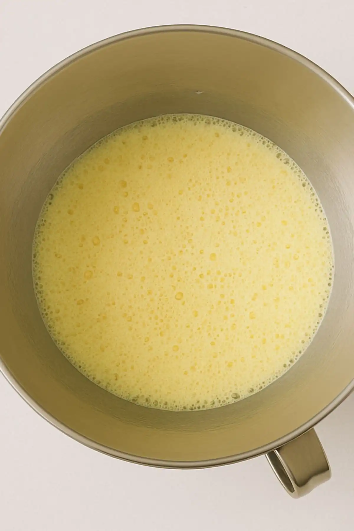 Whipped eggs and vanilla extract blended into creamed butter and sugar in a stainless steel bowl