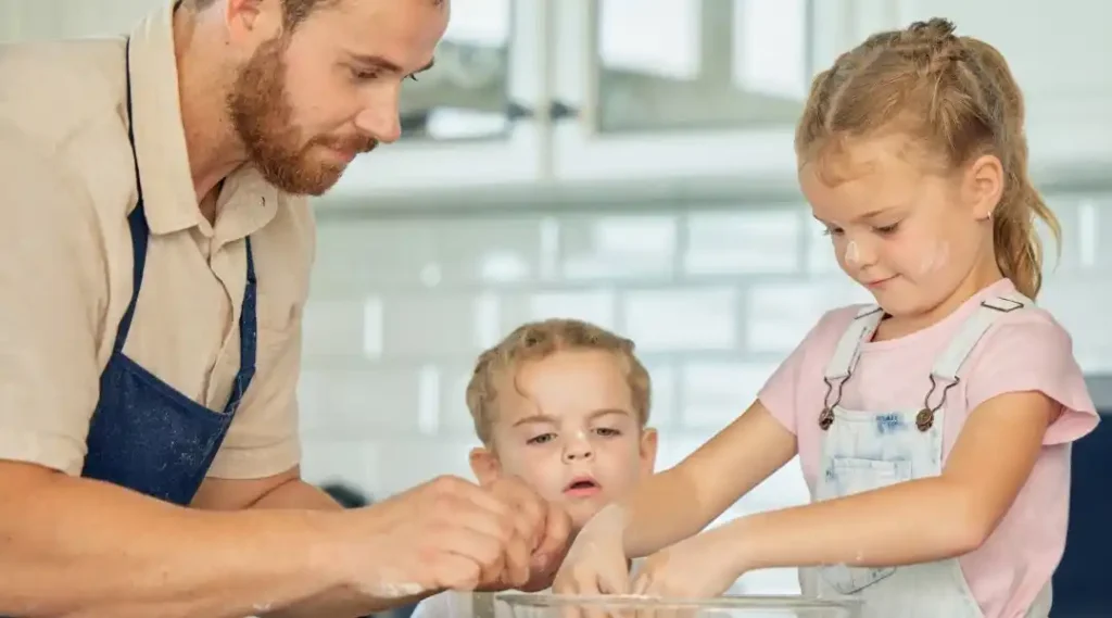 Dad cooking with his two daughters, making family memories in the kitchen with flour on their faces