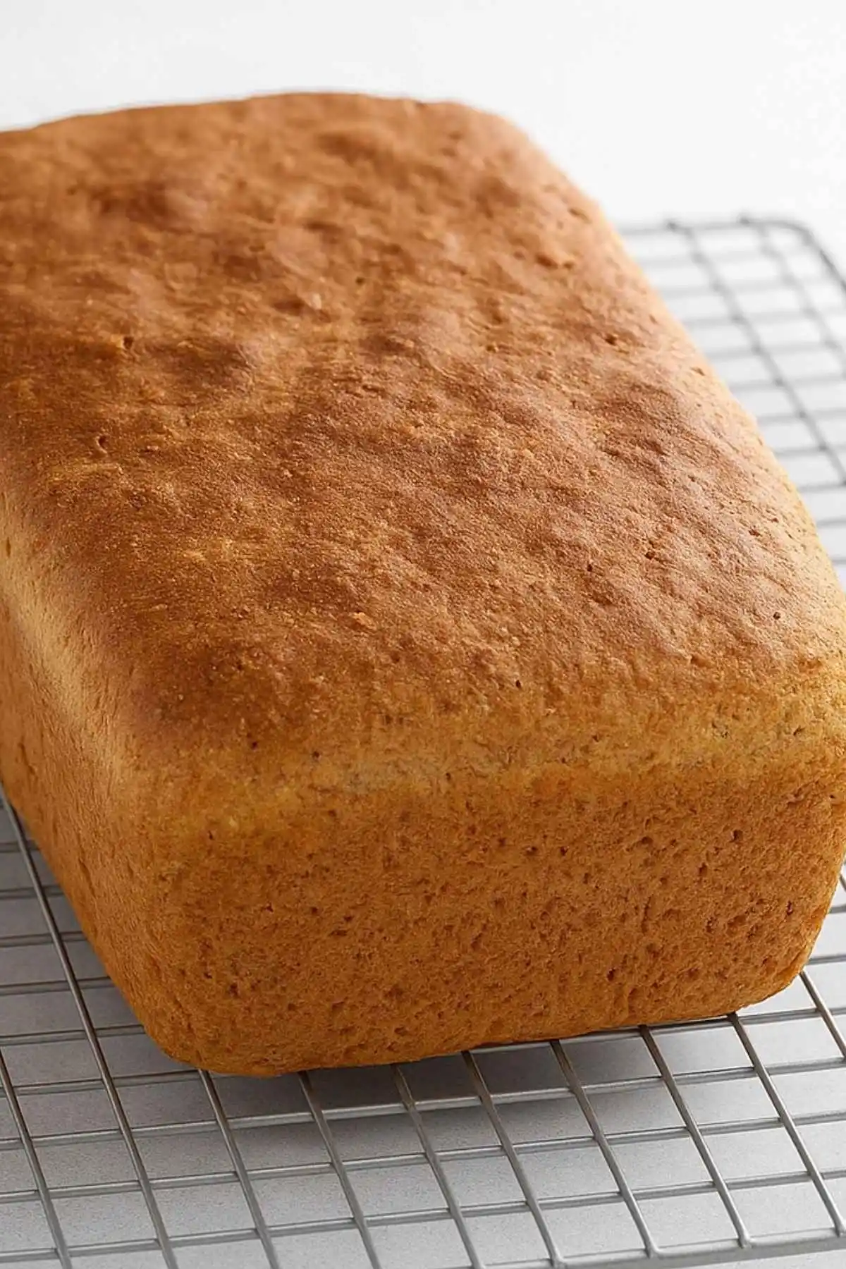 Loaf of gluten free and sugar free bread cooling on a wire rack with golden crust.