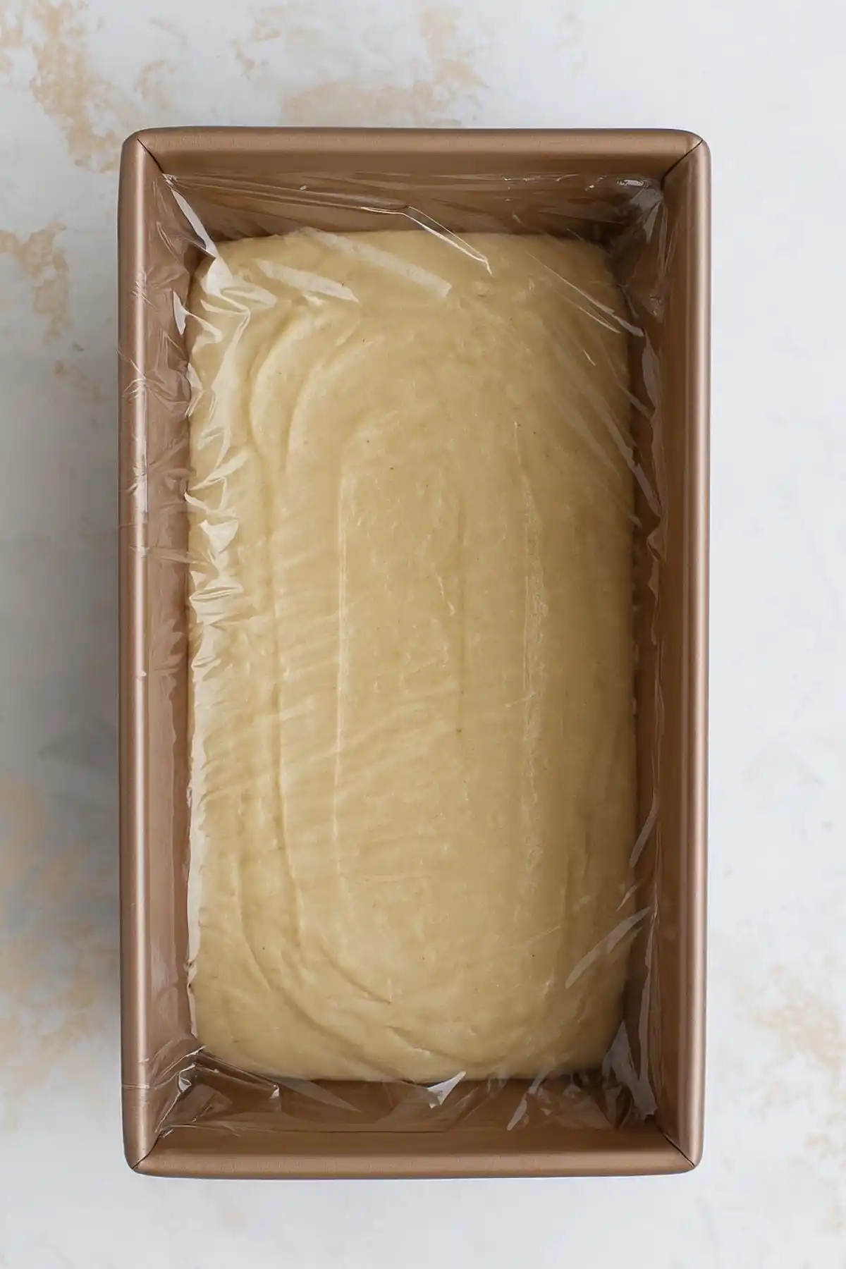 Covered loaf pan with gluten free bread batter resting before baking for improved texture.
